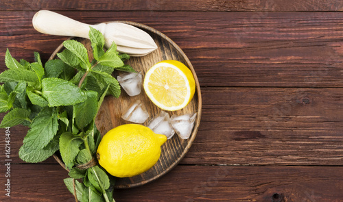 Ingredients for lemonade - lemon, mint, ice in wooden tray on a wooden background. Top view, copy space. Food background