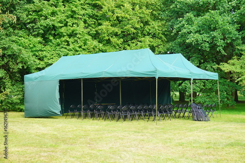 Green garden tent, garden pavilion. Rest area with chair and picnic tables and green tent installed on green lawn in a park 