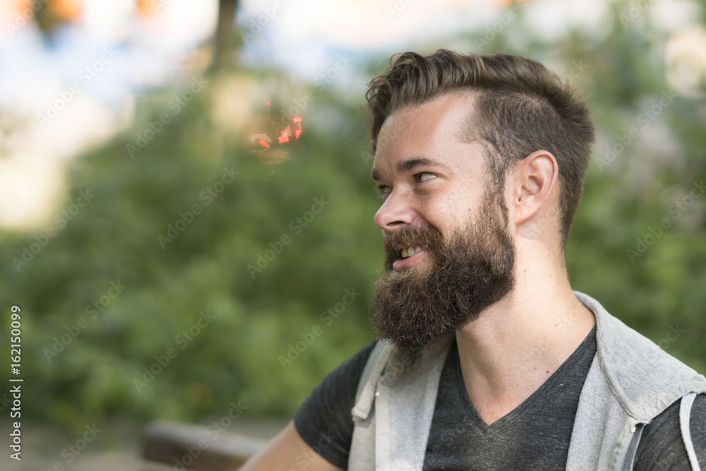 Profile portrait of a handsome smiling hipster guy with beard in park Profile portrait of a handsome smiling hipster guy with beard in park