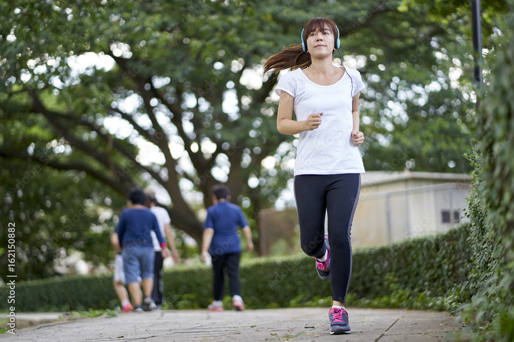 Women with headphones jogging and relaxing stroll in the park happy. Women with headphones jogging and relaxing stroll in the park happy.