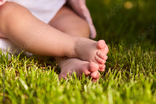 Small baby feet on the green grass at summer sunshiny day in the park. © Aleksey