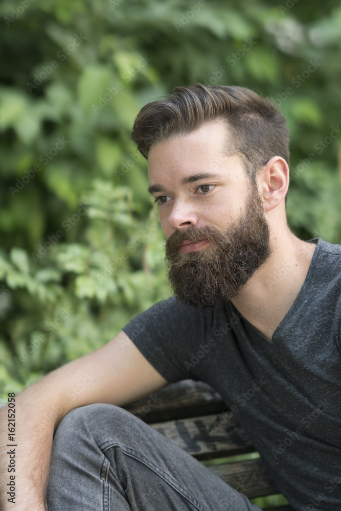Thoughtful bearded guy sitting on a bench in park Thoughtful bearded guy sitting on a bench in park
