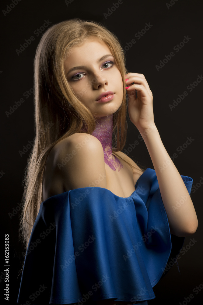 Stylish blonde woman with long lush hair and blue dress with naked shoulders