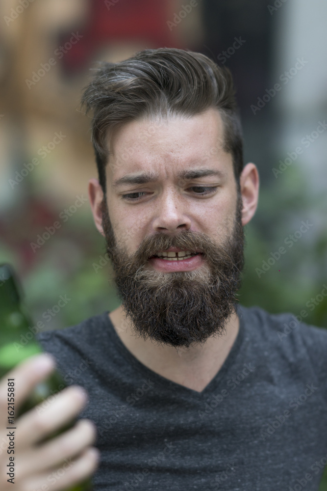 Handsome hipster holding a bottle of beer. Focus on his face on background Handsome hipster holding a bottle of beer. Focus on his face on background