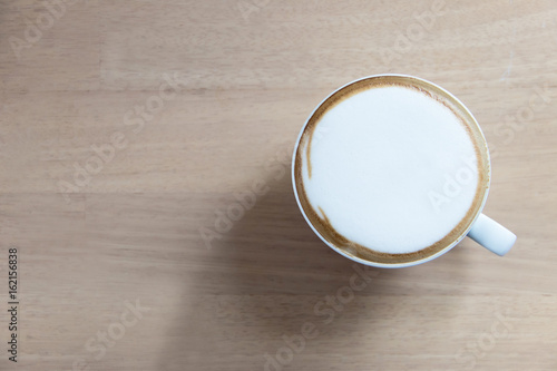 Hot cappuccino in white cup on wooden table with copy space