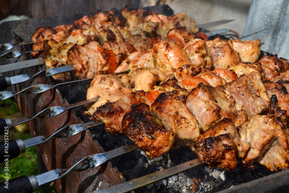Grilled kebab cooking on metal skewer closeup. Roasted meat cooked at barbecue. Traditional eastern dish, shish kebab. Grill on charcoal and flame, picnic