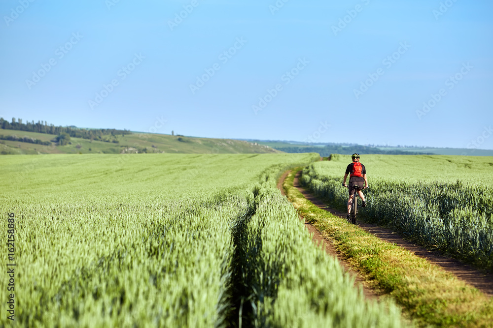 Rear view of the young cyclist with backpack cycling in the track of the field.