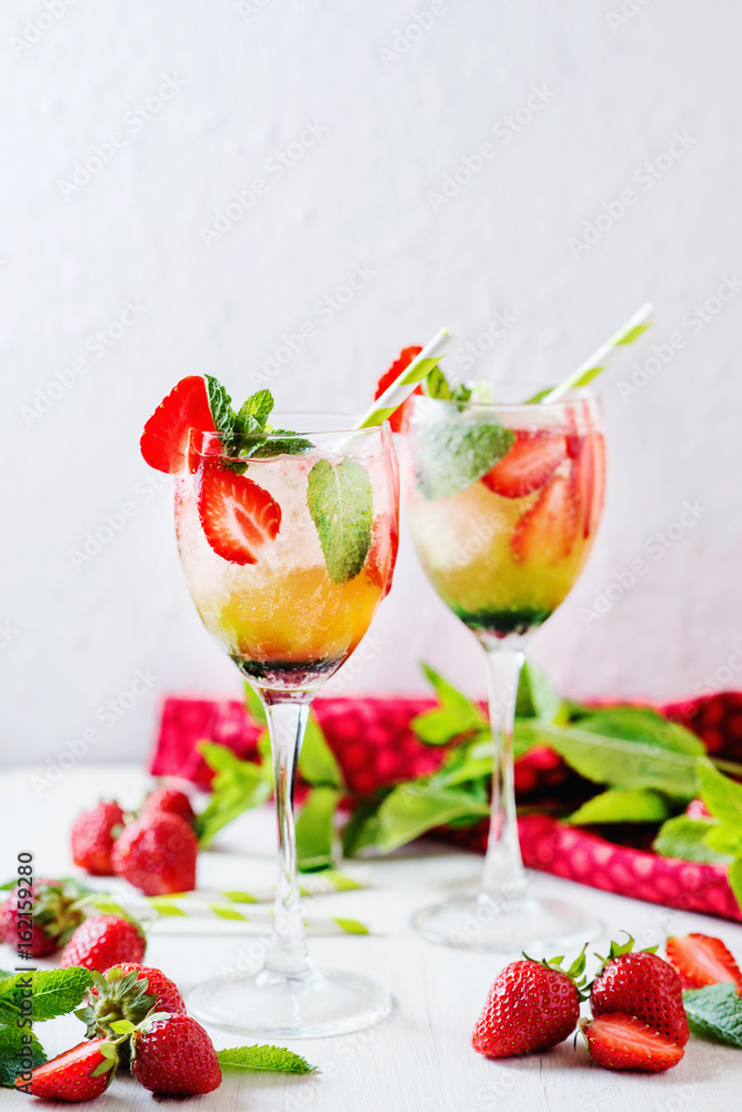 Alcoholic and non-alcoholic refreshing drinks, cold sparkling cocktail with ice, green mint and fresh strawberries in a beautiful glass on a light background Alcoholic and non-alcoholic refreshing drinks, cold sparkling cocktail with ice, green mint and fresh strawberries in a beautiful glass on a light background