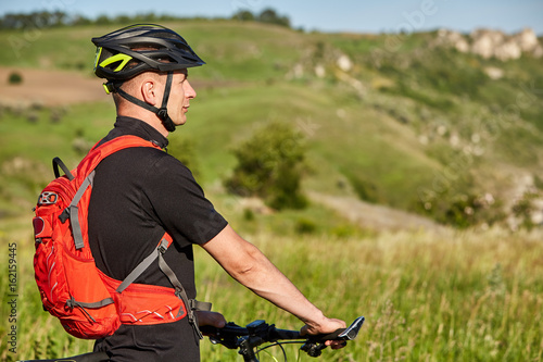 Close-up of the cyclist standing on the hill on a background with beautiful landscape.