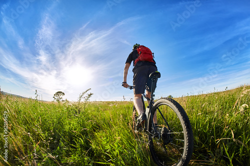 Young cyclist riding mountain bicyclist against beautiful sunrise in the countryside.