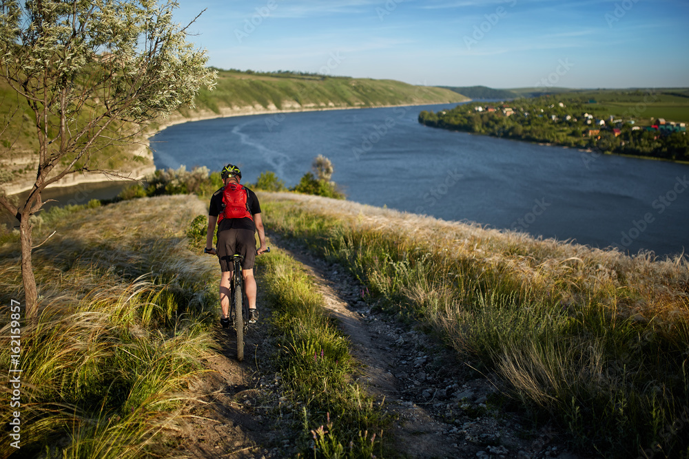 Young cyclist riding mountain bike uphill along a country road above river.