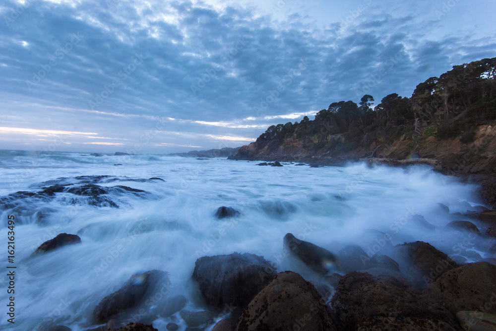 Dramatic ocean tide splashing water by rocky shore during sunset in California Dramatic ocean tide splashing water by rocky shore during sunset in California
