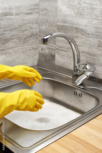 Hands in gloves against kitchen sink full of foam