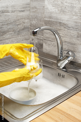 Hands in gloves washing drinking glass under running tap water