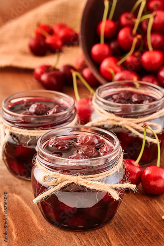 Cherry jam on wooden background in the jars