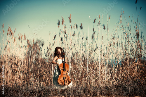Girl with a cello in a tall grass