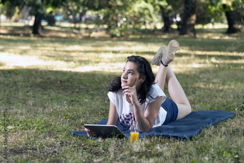 She is lying on the grass and using a tablet