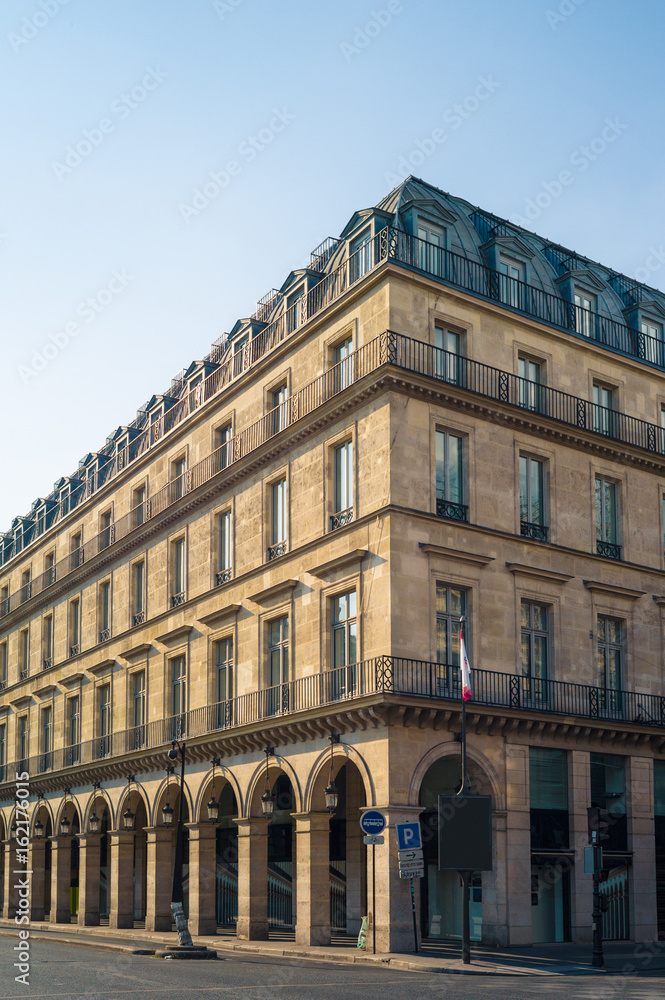 A typical Haussmann style building in Paris with balconies, arches and shops under a warm light of late afternoon.