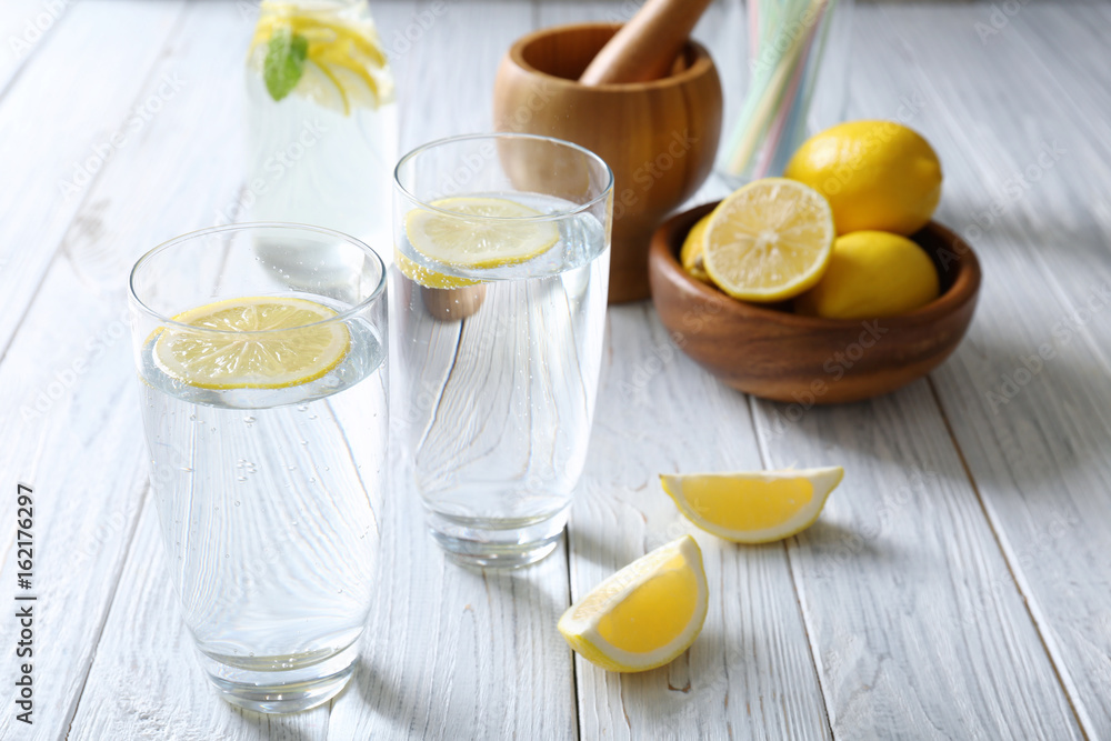 Glasses with cold lemon water on light wooden table Glasses with cold lemon water on light wooden table