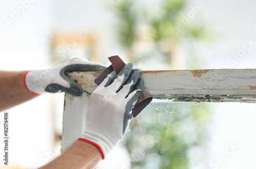 Worker grinding surface of old window frame with abrasive paper, closeup