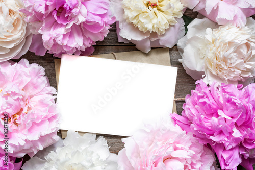 blank greeting card or wedding invitation and envelope in frame of tender peonies flowers