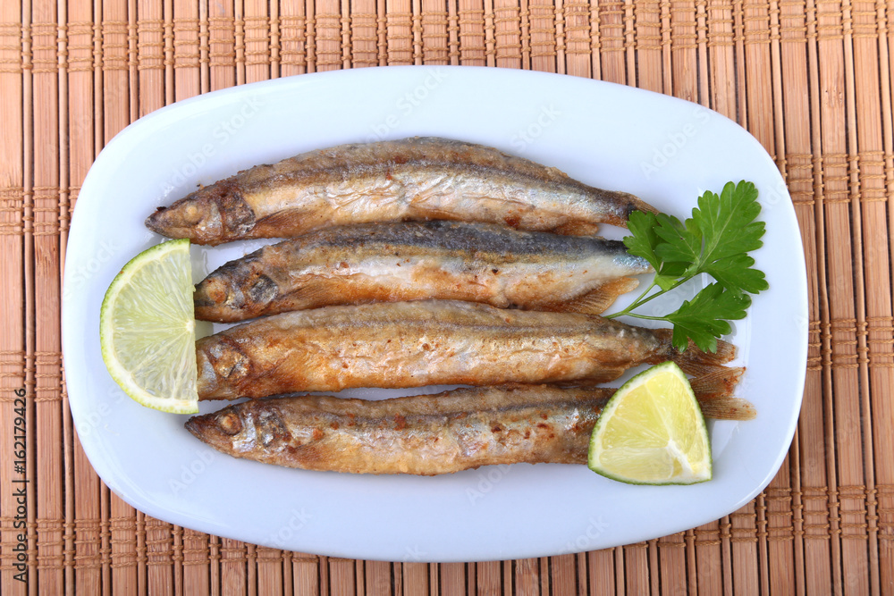 Deep frying small fish capelin and sliced lemon on white plate. Good snack to beer. Deep frying small fish capelin and sliced lemon on white plate. Good snack to beer.