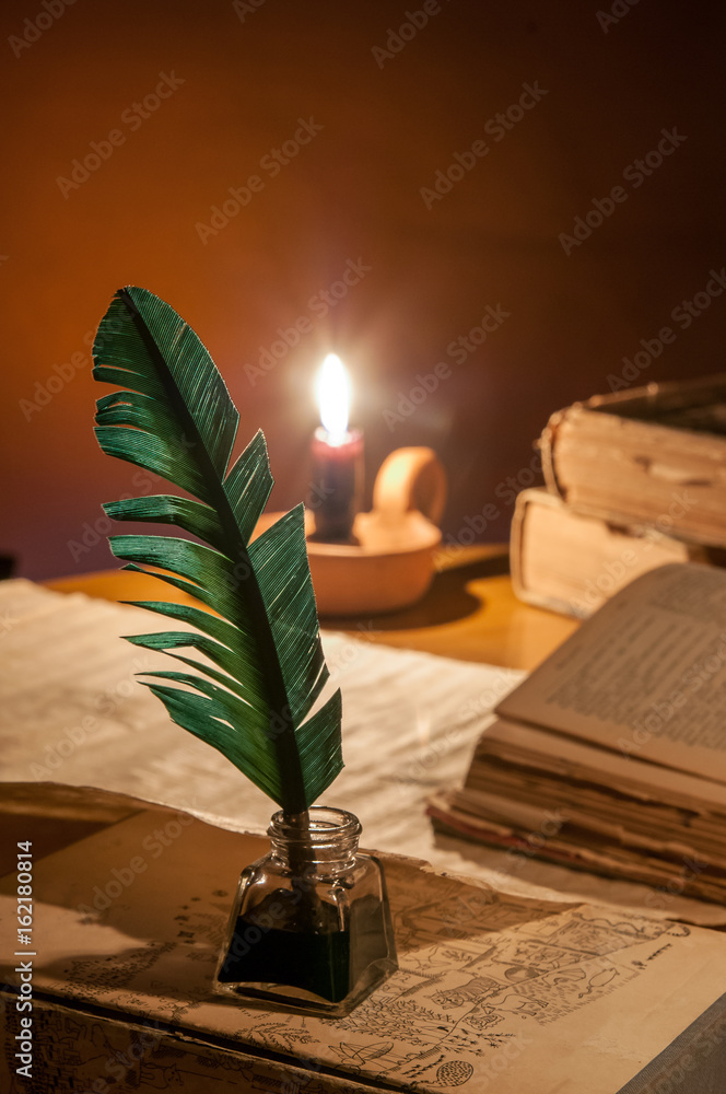 Quill pen, old papers and books by candle light
