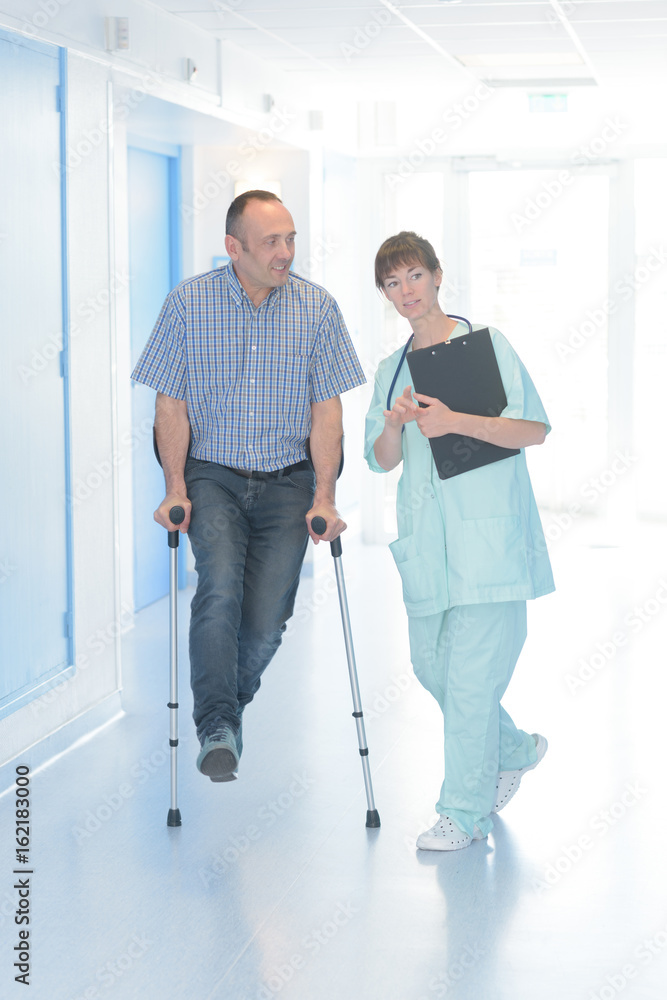 nurse helping man with crutches in hospital corridor nurse helping man with crutches in hospital corridor