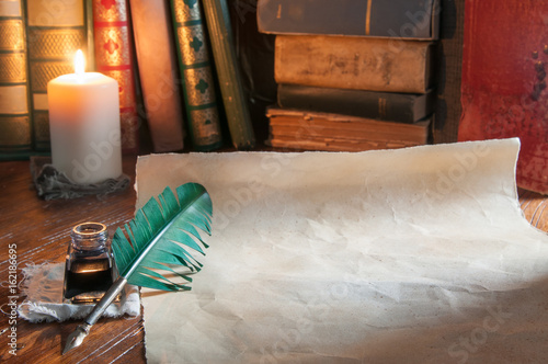 Quill pen, old papers and books by candle light