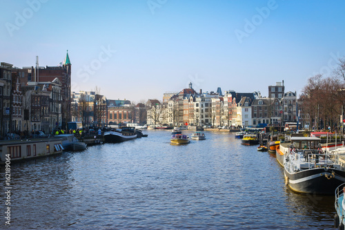 Boats are cruising through the water canal in Amsterdam city during the day