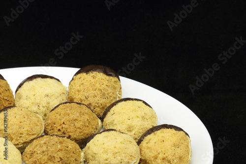 Homemade Christmas cookies, special Czech sweets on white plate, isolated on black. Pastry, cookies, biscuit, cracker with spice (cinnamon) and nuts (walnuts), half dipped in chocolate photo