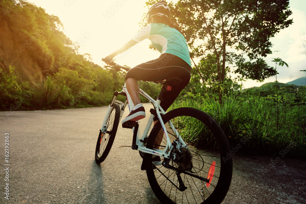 Naklejka premium woman cyclist cycling on sunrise forest trail
