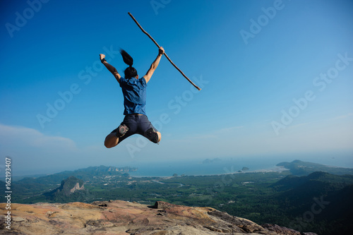 successful woman jumping on rocky mountain peak