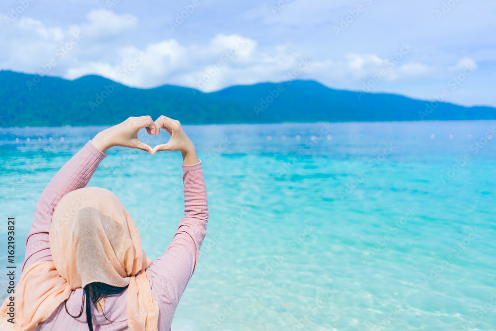 Beautiful of happy young woman  lift hand showing heart shape at lipe thailand island with the turquoise ocean water.