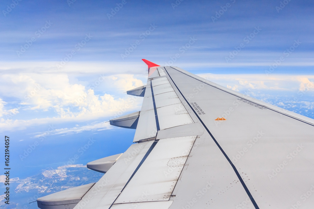 Aircraft wing flying above the clouds in blue sky. from its windows