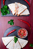 Mexican quesadilla with salsa on black slate stone plate on red wooden background. Chili pepper. Top view.