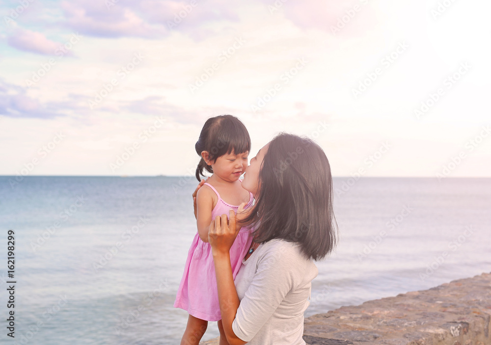 mother and kid girl kissing with natural emotion smiling on sea background in the evening. mother and kid girl kissing with natural emotion smiling on sea background in the evening.
