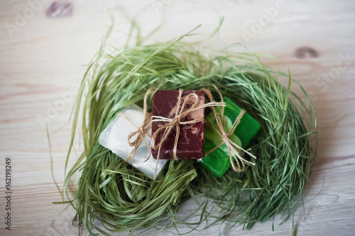 Bathroom accessories. Body care. A multi-colored natural soap, tied with string, lies in natural grass. Cosmetic pieces of soap on a light white background in the grass. Spa treatments