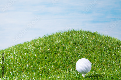 White ball lies on a peg stuck into a lawn for a game of golf, against a blue sky background