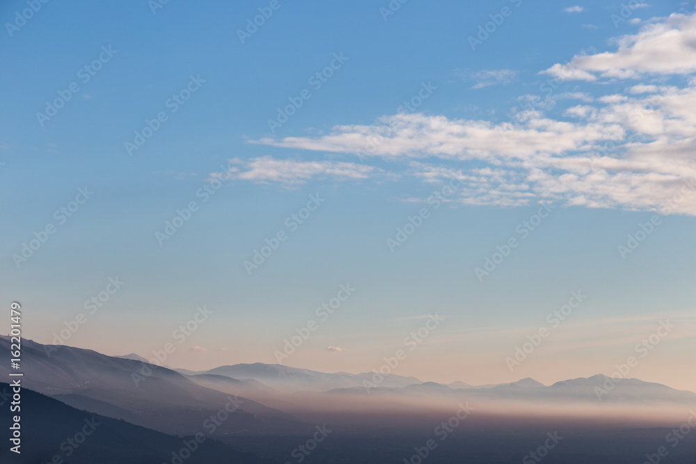 View of a valley at golden hour, with mist between the hills and mountains, and a blue sky with white clouds