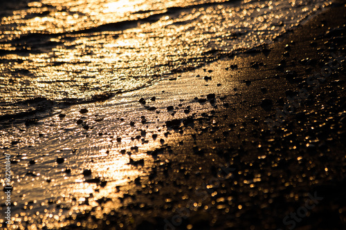 A close up of a shore at sunset, with light reflections on water and small stones