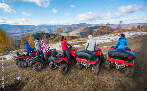 Fényképezés Rear view of a group of people on red quad bikes at hill enjoying open views of