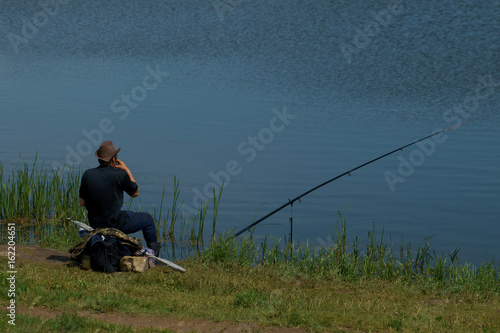 fisherman with fishing rod catching fish, sitting riverside