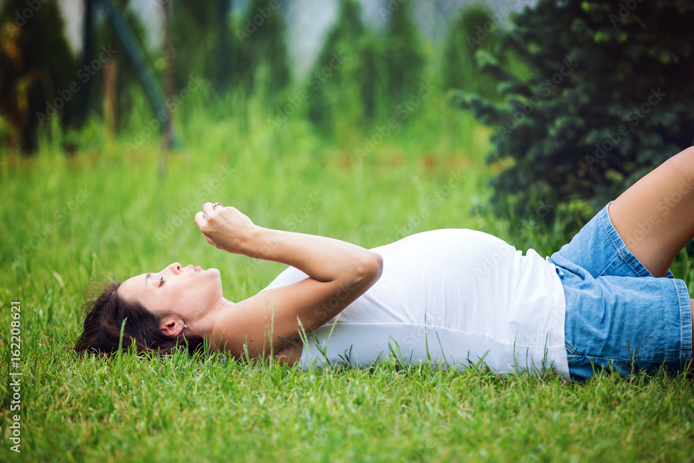 Beautiful young pregnant woman, lying down in the grass, making soap bubbles Beautiful young pregnant woman, lying down in the grass, making soap bubbles