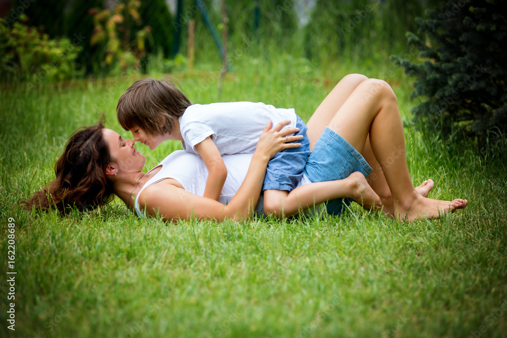 Beautiful young pregnant woman and her older child, lying down in the grass Beautiful young pregnant woman and her older child, lying down in the grass