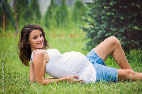 Beautiful young pregnant woman, lying down in the grass, making soap bubbles