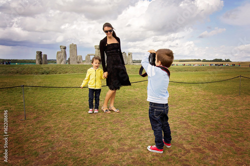 Young child, boy, taking pic of his mom and brother with digital camera at Stonehenge