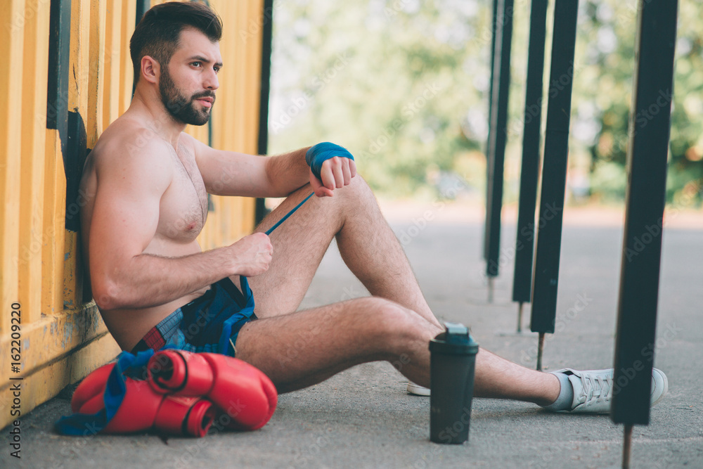man pulls boxing bandages Sits on the asphalt. gay in sportswear is  preparing for sparring. Boxing ring under the open sky. outdoors fighting  Stock Photo | Adobe Stock