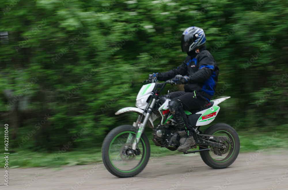 Motorcyclist in blue outfit rides against the backdrop of foliage on the off-road