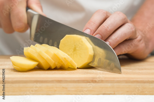 Chef's hands with knife cutting the potato on the wooden board. Preparation for cooking. Healthy eating and lifestyle.